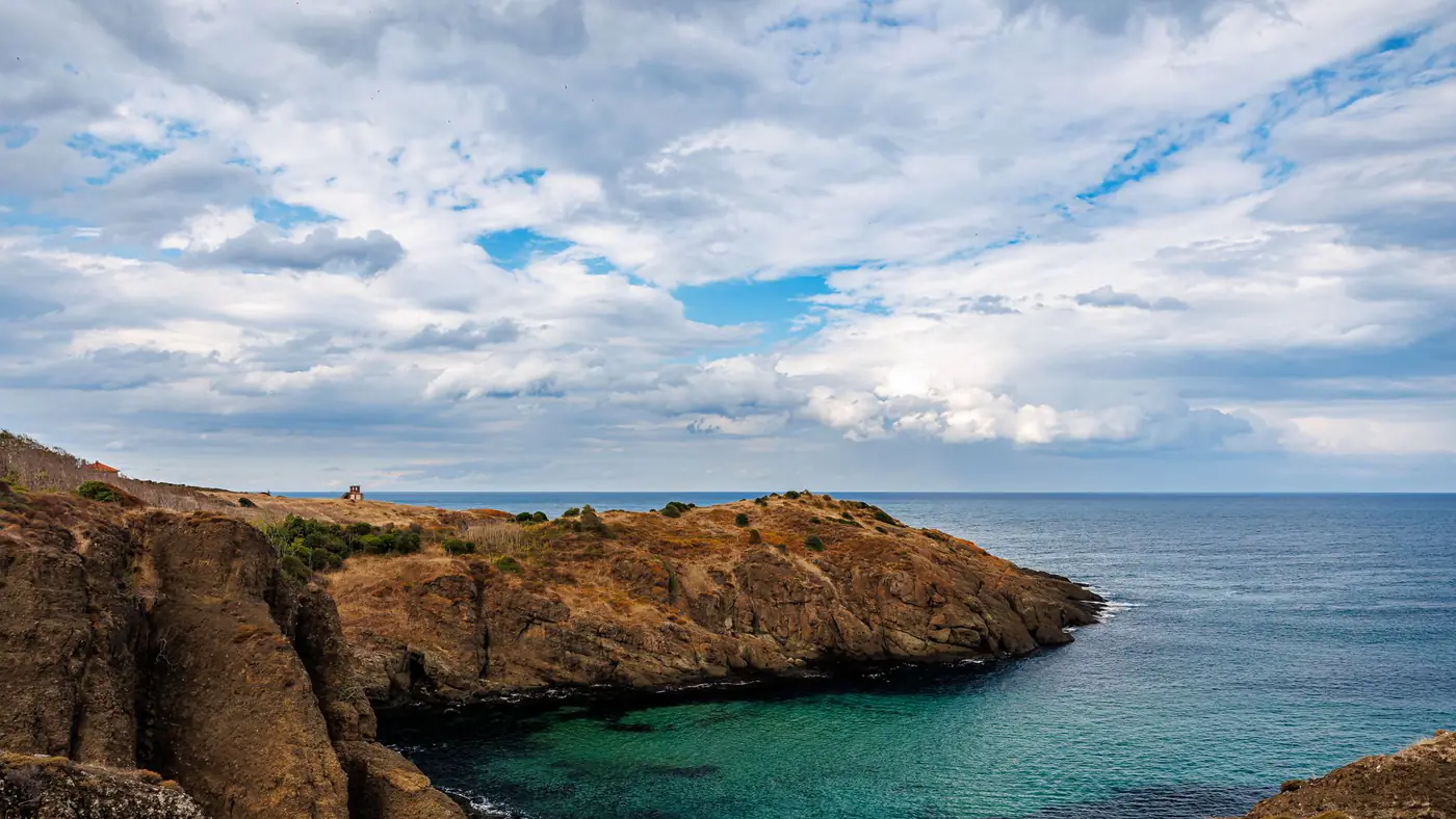 Dramatic coastal view featuring rocky cliffs, turquoise waters, and dynamic clouds.