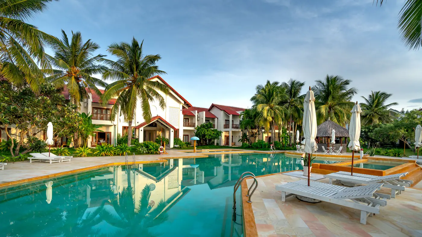 A serene view of a luxury resort with a swimming pool surrounded by palm trees.