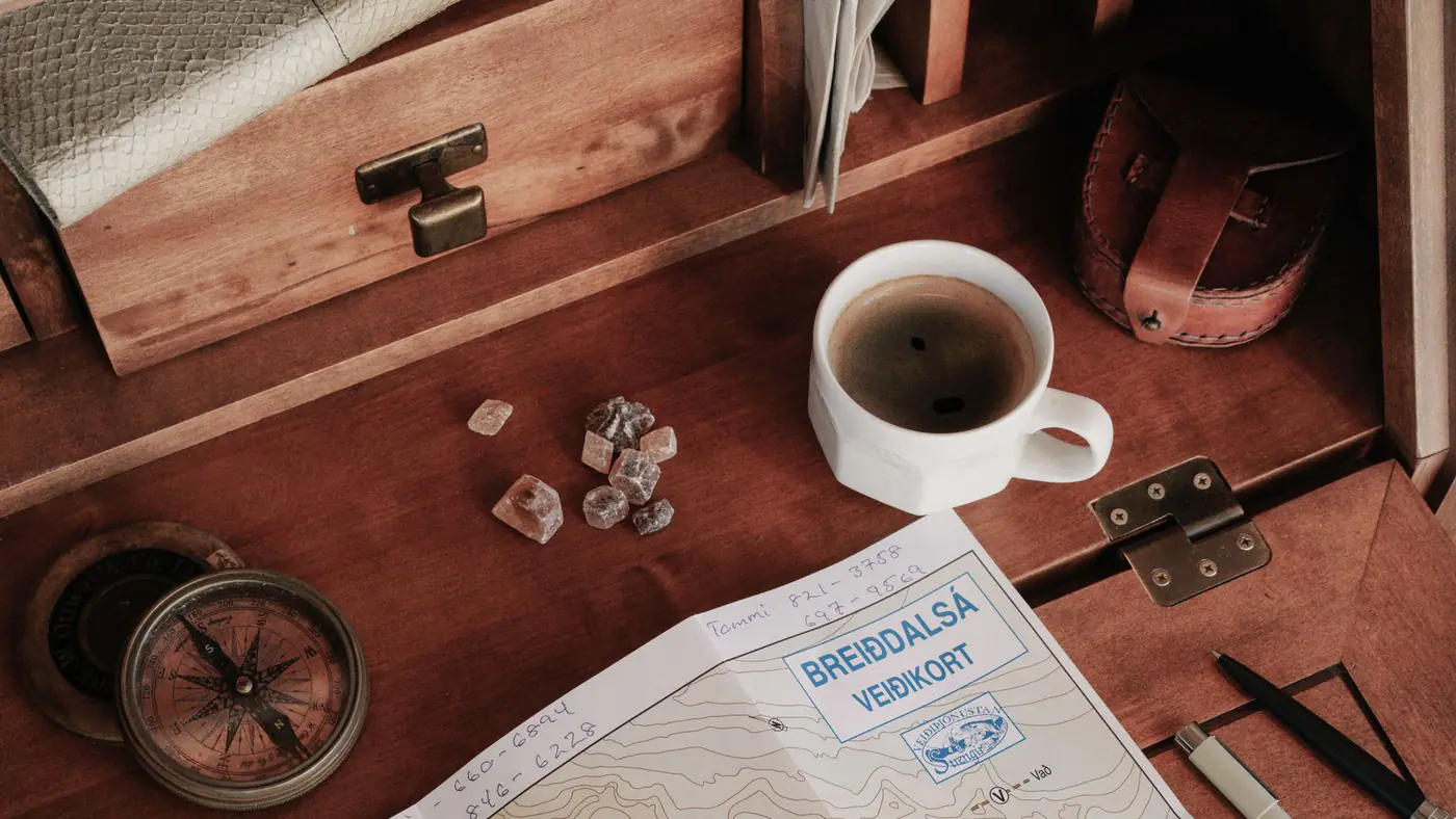 A top-down view of a rustic workspace featuring a map, compass, and a cup of coffee.
