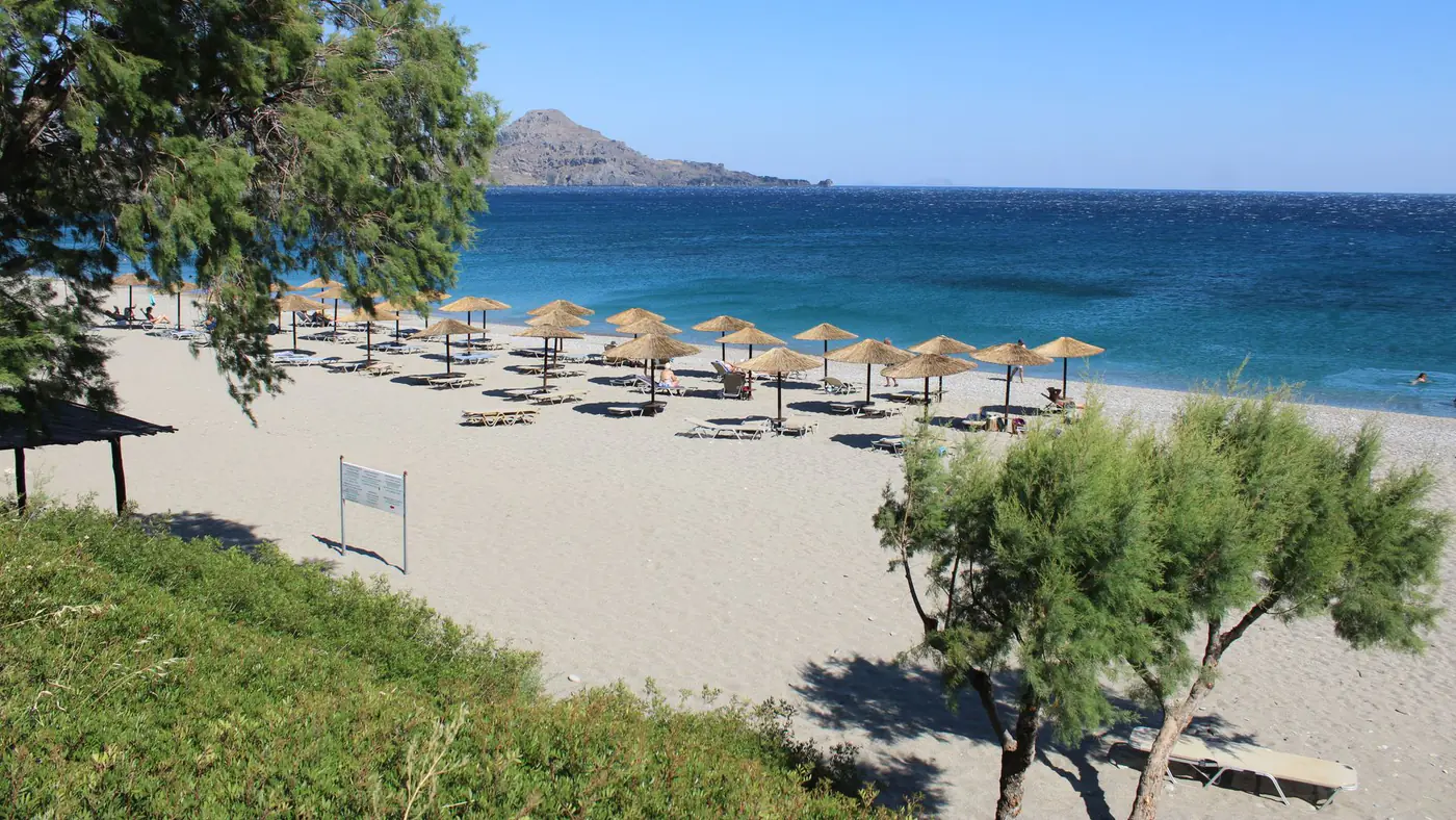 Tranquil sandy beach in Crete, Greece with sun umbrellas and clear blue sea.