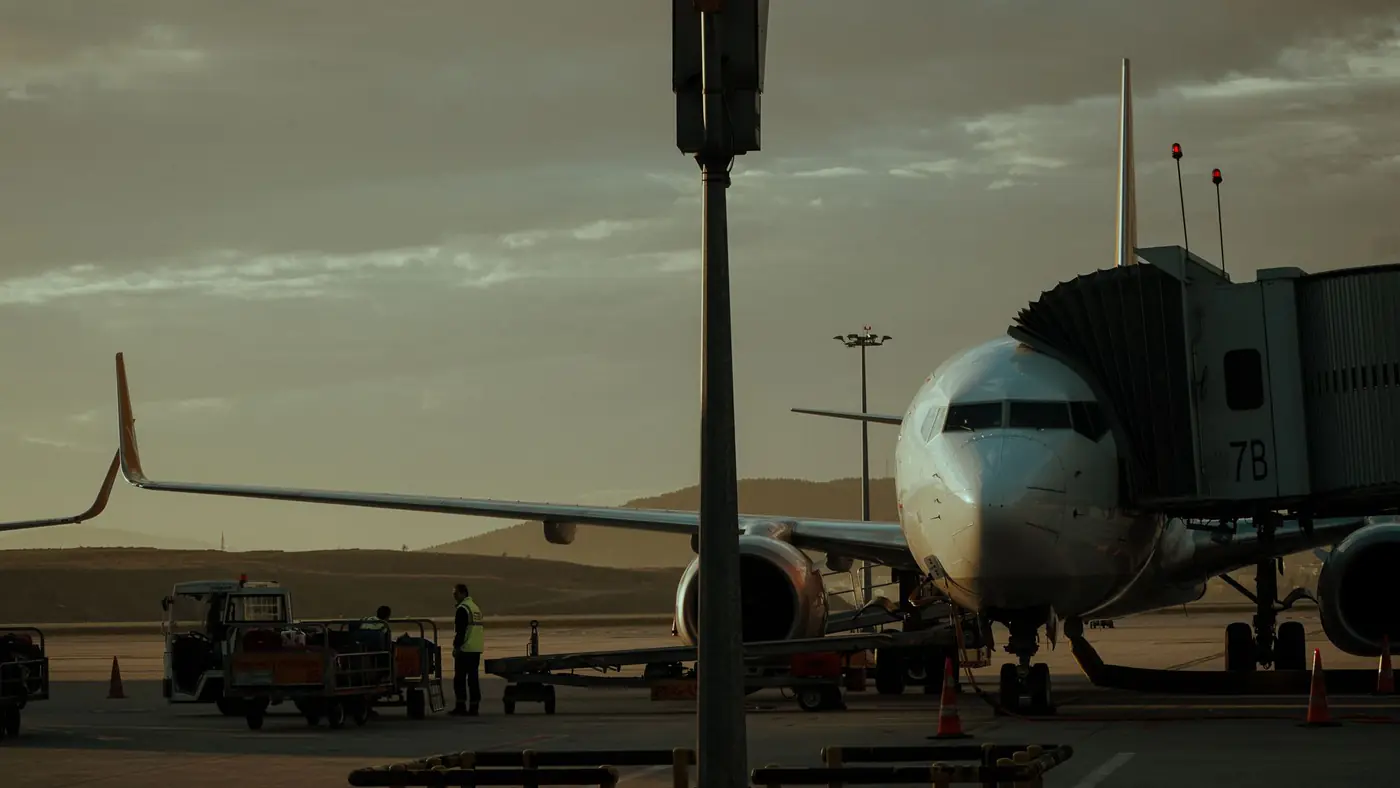 A commercial airplane at an airport gate during sunset with ground crew preparing for departure.