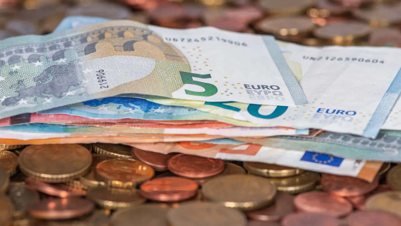 Stack of euro banknotes and scattered coins symbolizing wealth and finance.