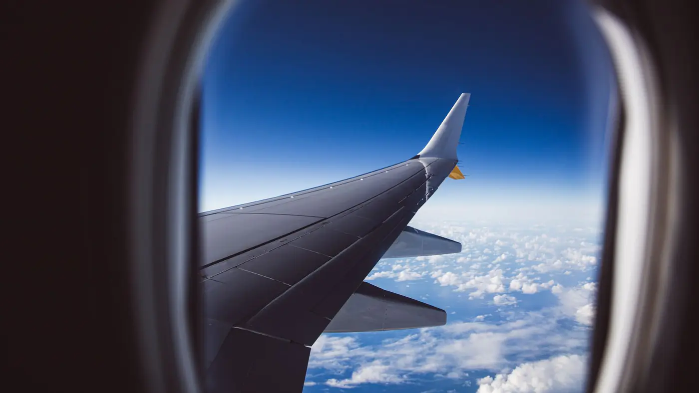 A view from an airplane window showing the wing and clouds below, captured in daylight.