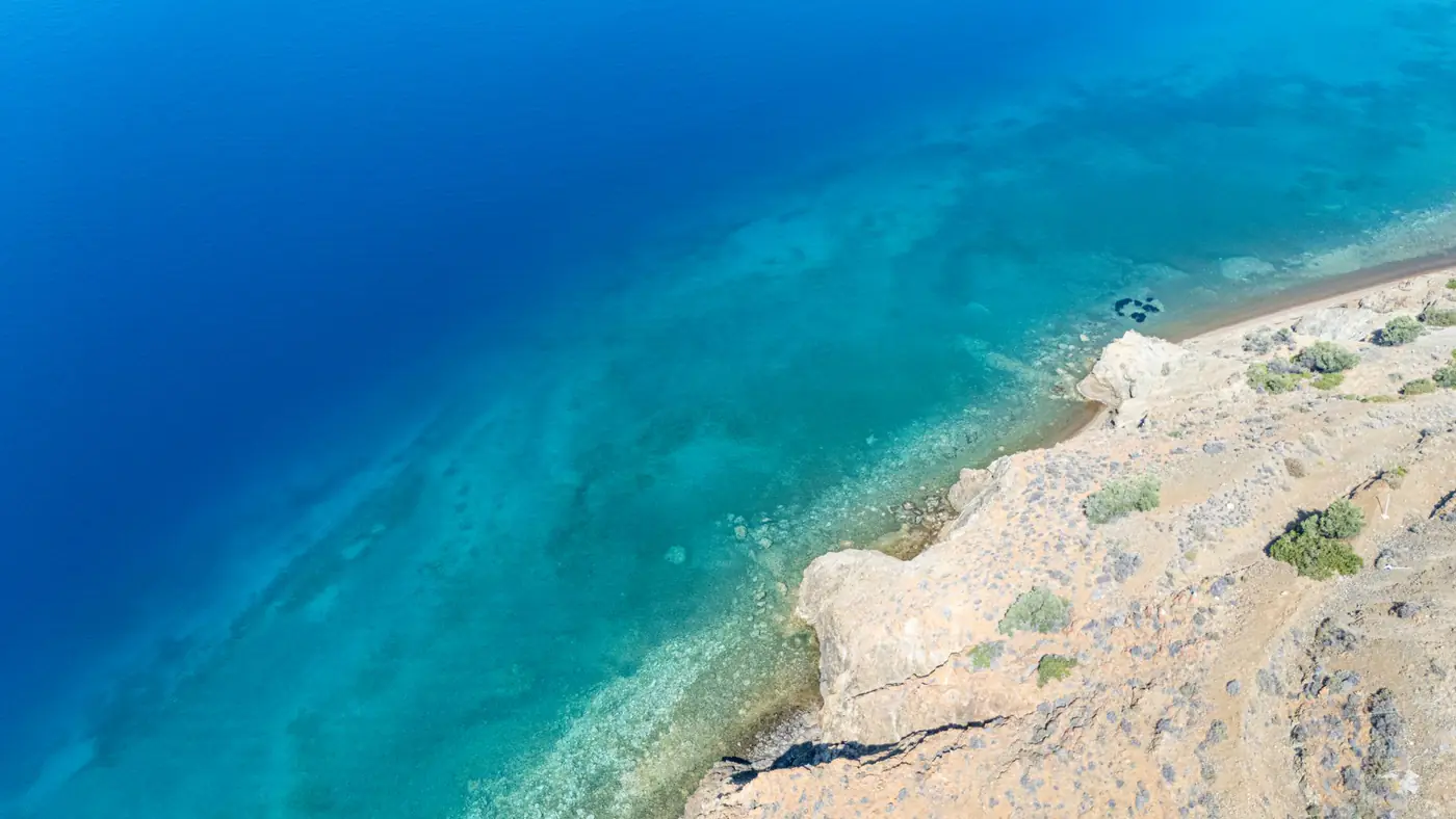 Stunning aerial view of rocky shoreline with clear turquoise waters in Greece.
