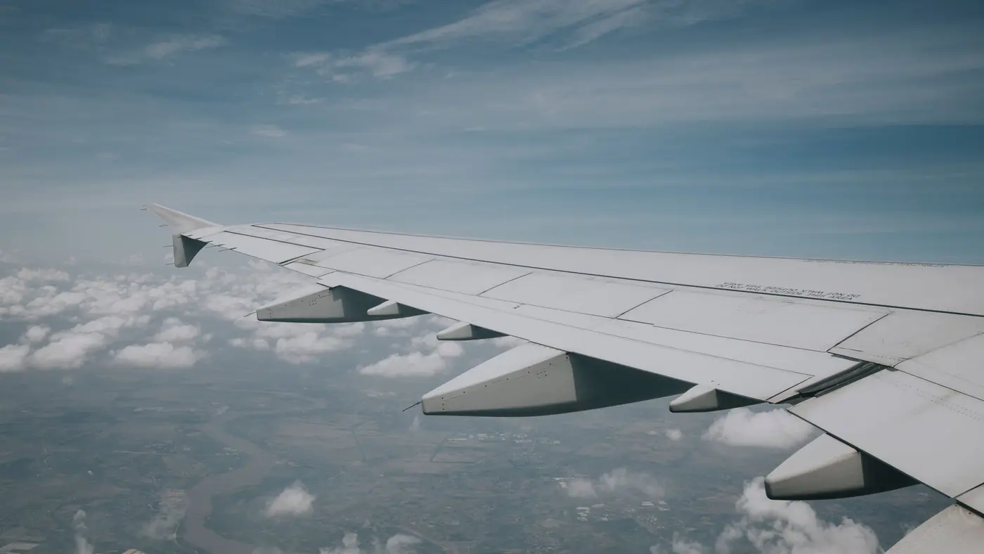 Aerial view from airplane window showing wing and clouds beneath a clear blue sky.