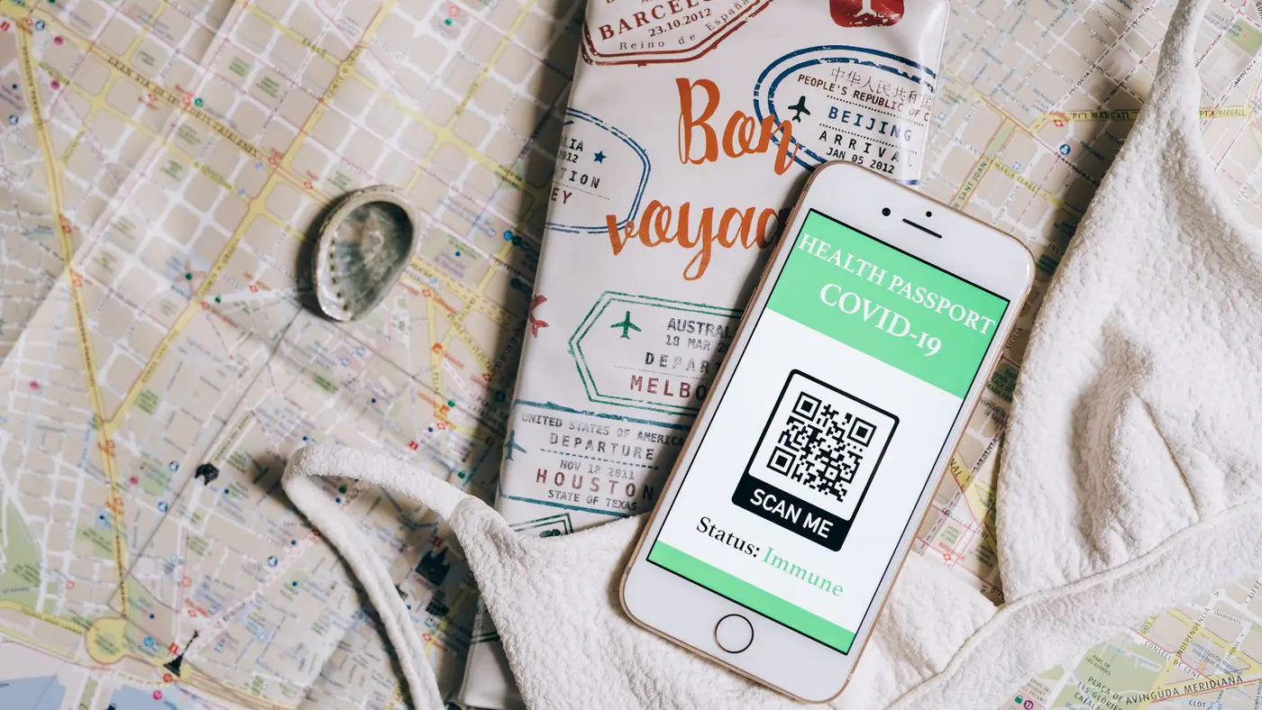 Smartphone displaying a health passport with QR code on a travel map and passport cover.