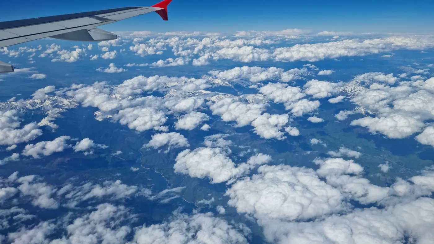 A breathtaking view of clouds and mountains from an airplane window, showcasing a serene and vast sky.