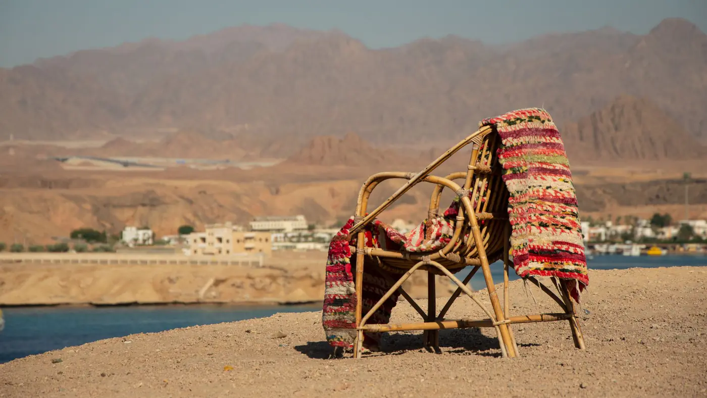 A cozy rattan chair with a colorful rug on a sandy beach, ideal for a serene vacation.
