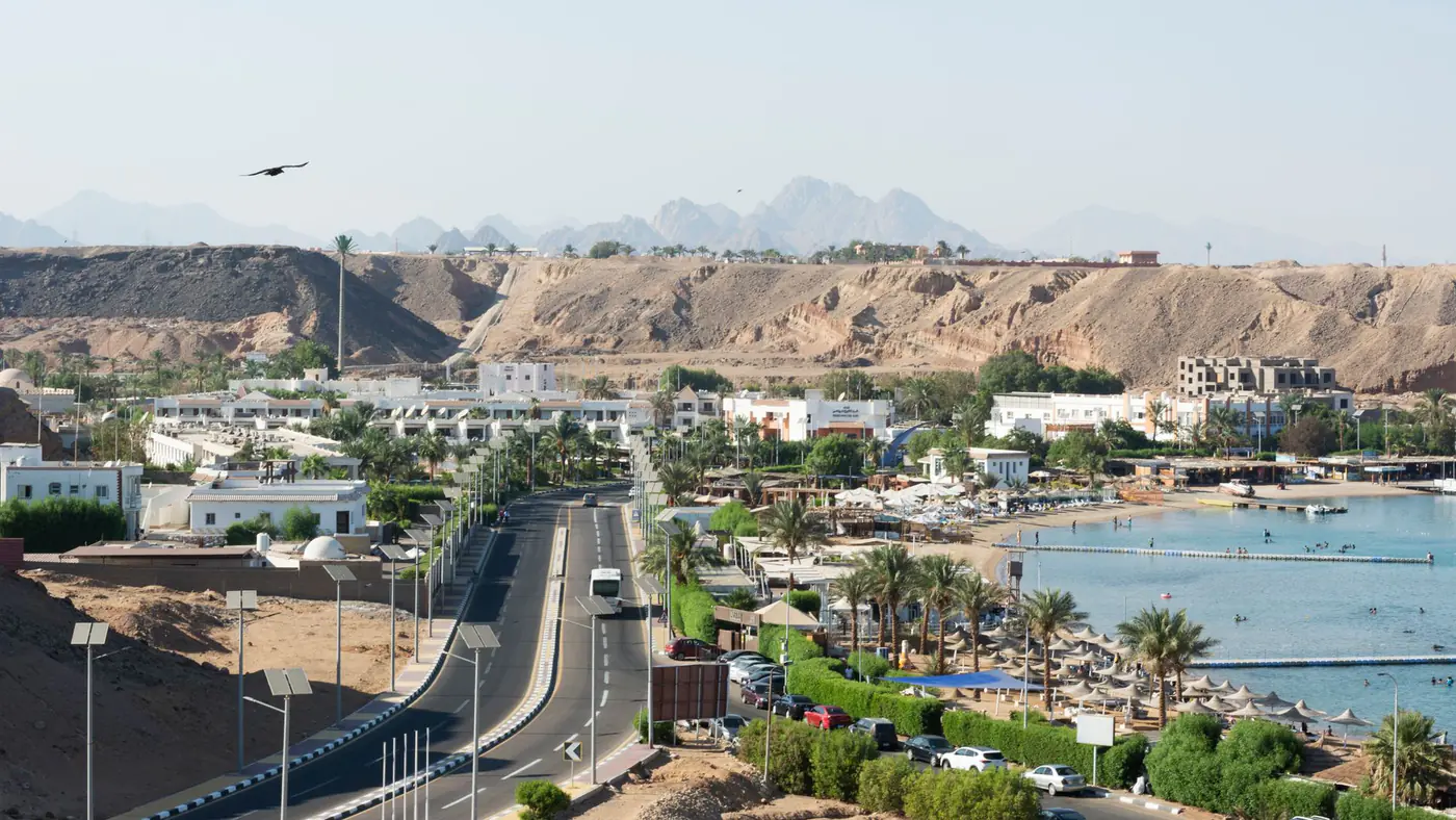 A panoramic aerial view of the Sharm El Sheikh coastline and surrounding cityscape, featuring sandy desert hills.