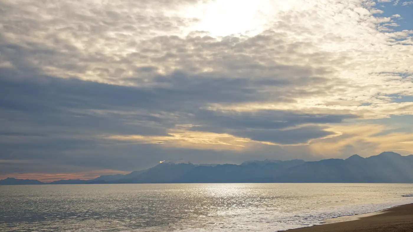 Serene view of Antalya's coast with dramatic clouds and a beautiful sunset over the sea.