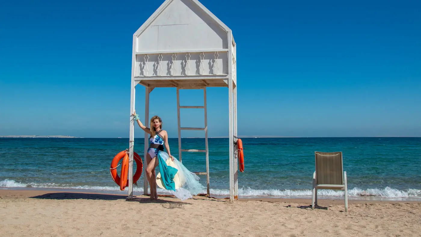 Woman in swimsuit near lifeguard tower by ocean on sunny beach. Perfect summer day.