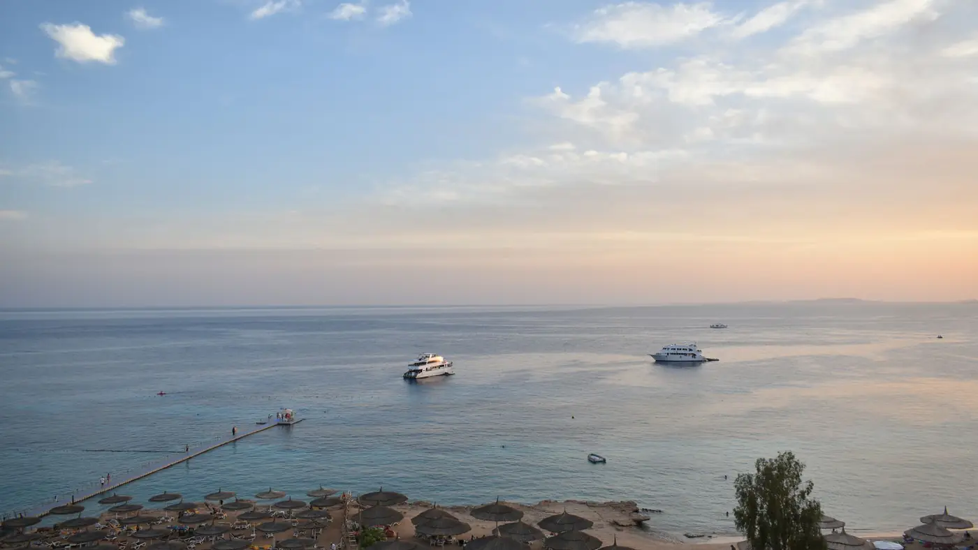 Stunning aerial view of Sharm El Sheikh's beach and sea during sunset with boats and parasols.