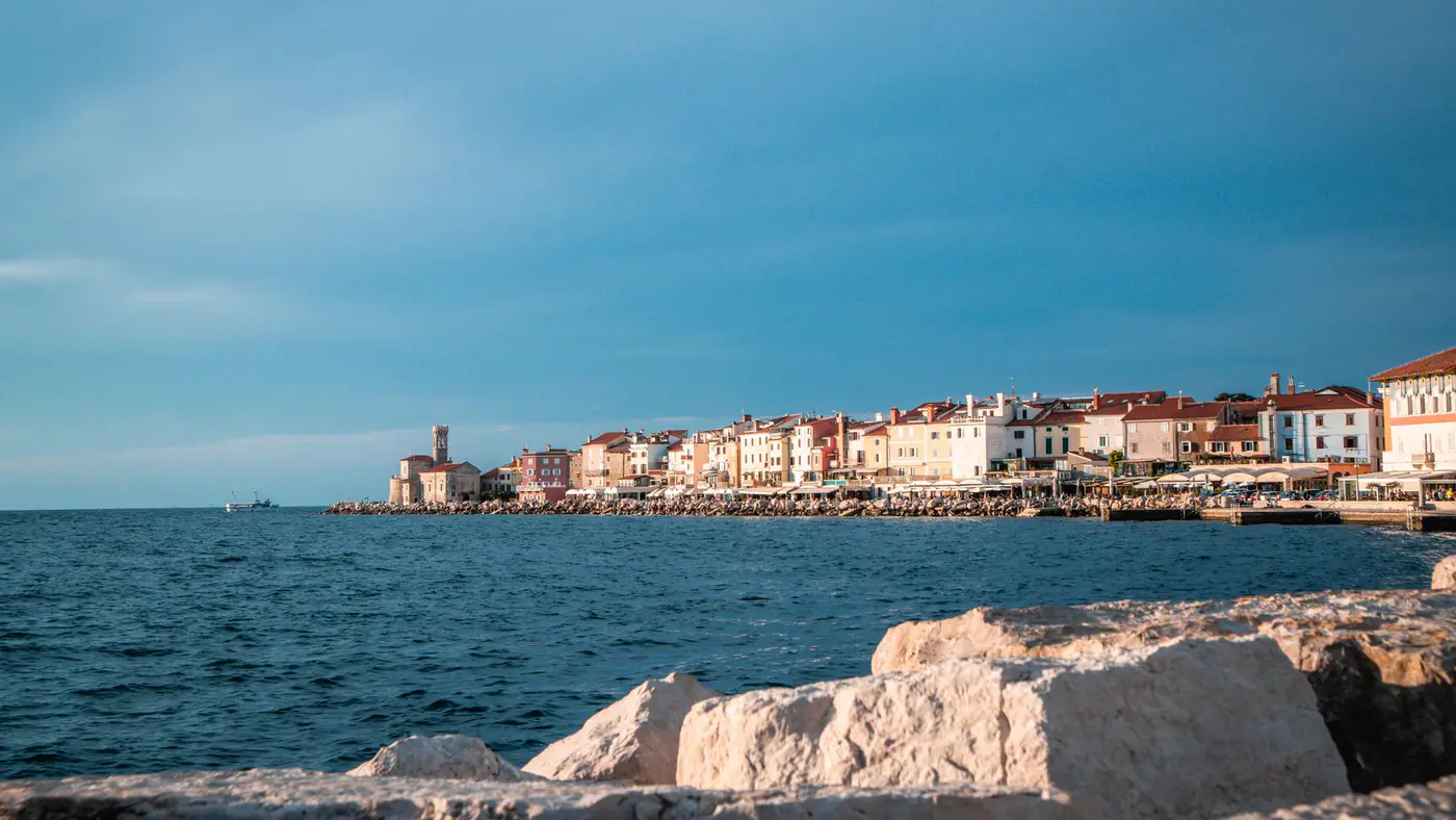 Scenic coastal view of a historic town with vibrant buildings along the shoreline, under a bright sky.
