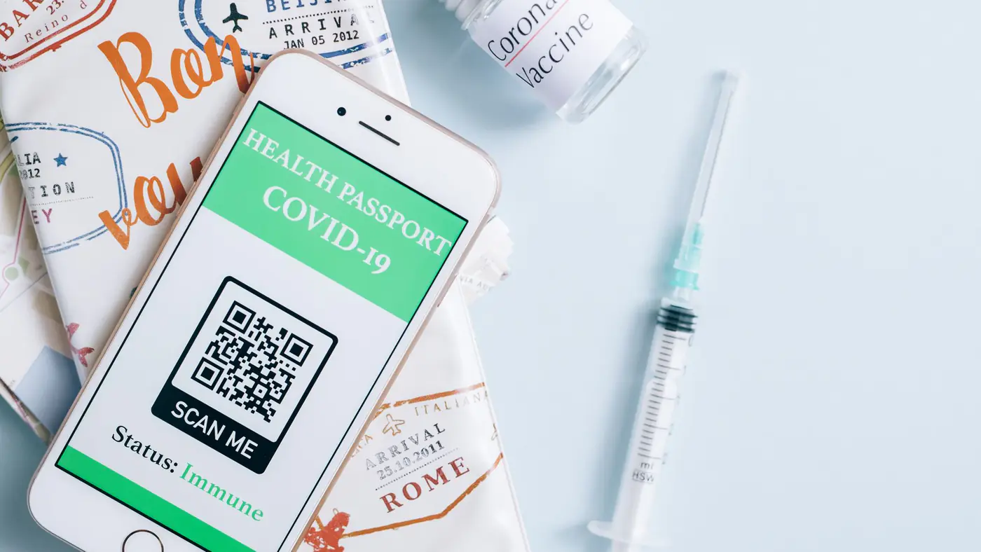 Image of a smartphone displaying a COVID-19 health passport next to a vaccine vial and syringe, ready for travel.