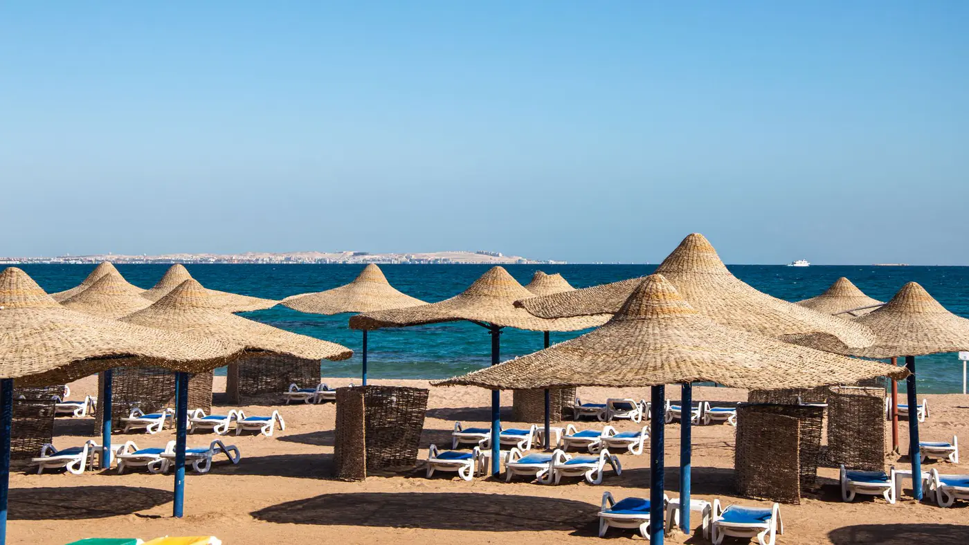 Wide view of a beach lined with straw umbrellas, sun loungers, and a calm blue sea.