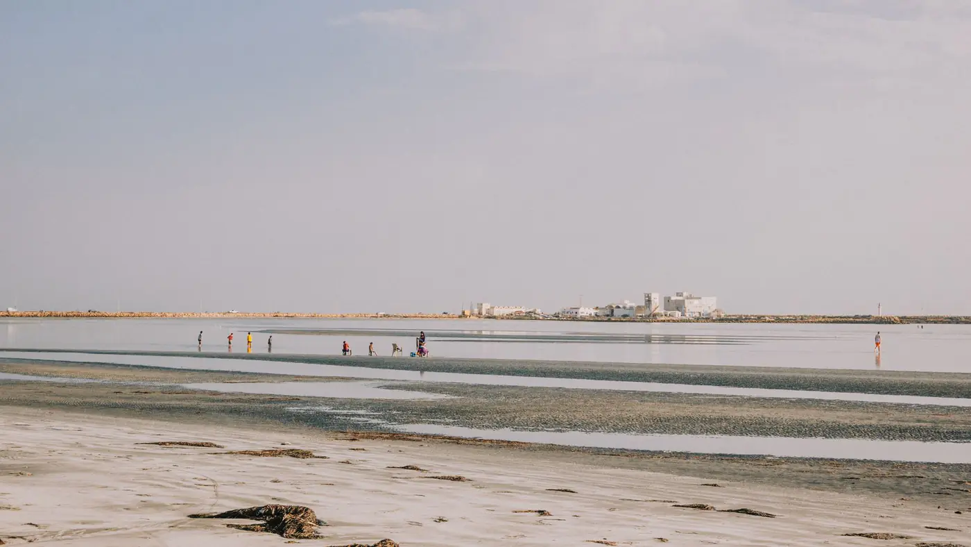 Tranquil beach landscape with people walking along the shore under a clear sky.