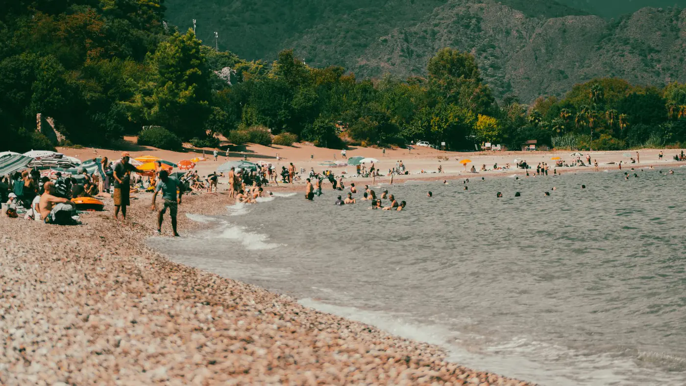 People enjoy a lively summer day at a picturesque pebbly beach with stunning mountain views.
