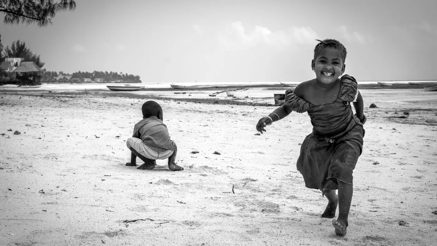 Happy children running and playing on a Zanzibar beach in black and white.