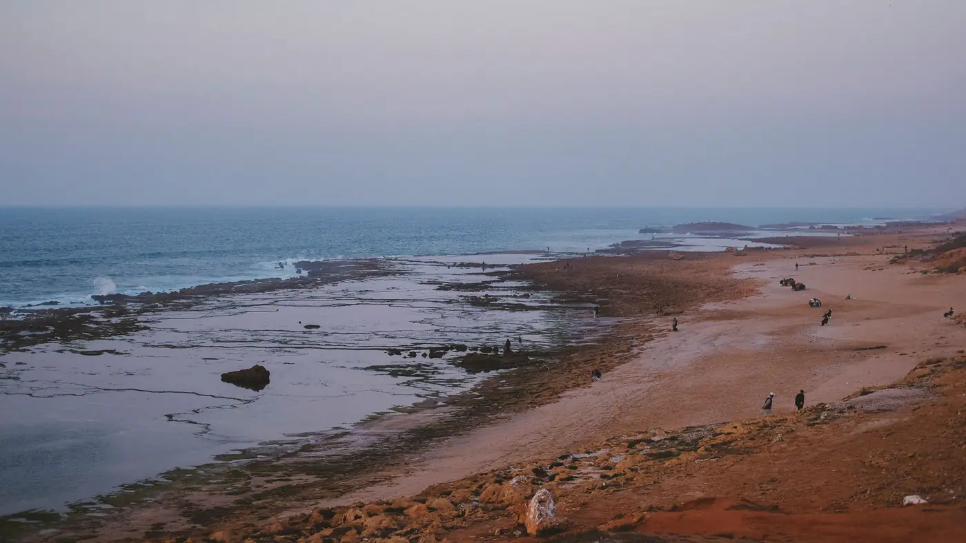 Tranquil sunset view over Oudayas Beach in Rabat, Morocco with scattered visitors along the shore.