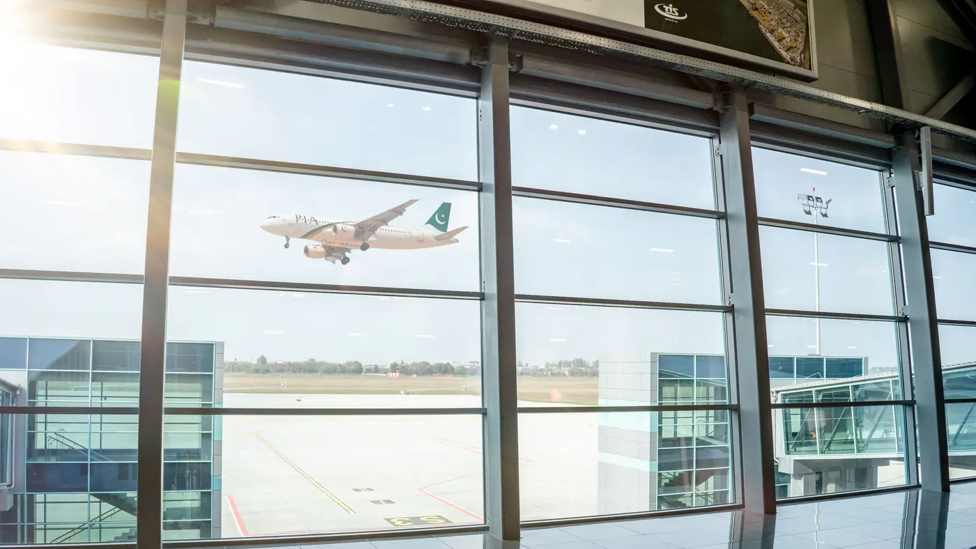 A plane in flight seen through airport terminal windows, reflecting air travel excitement.