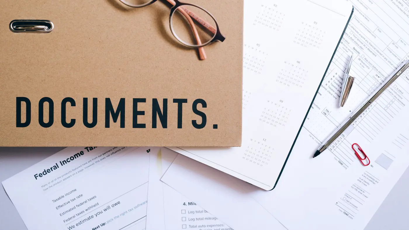 Flat lay of office supplies including documents, calendar, and eyeglasses on a desk.