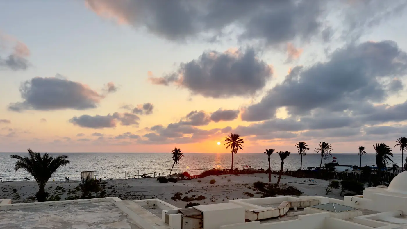 Beautiful sunset view over a beach in Médenine, Tunisia, with palm trees and ocean.