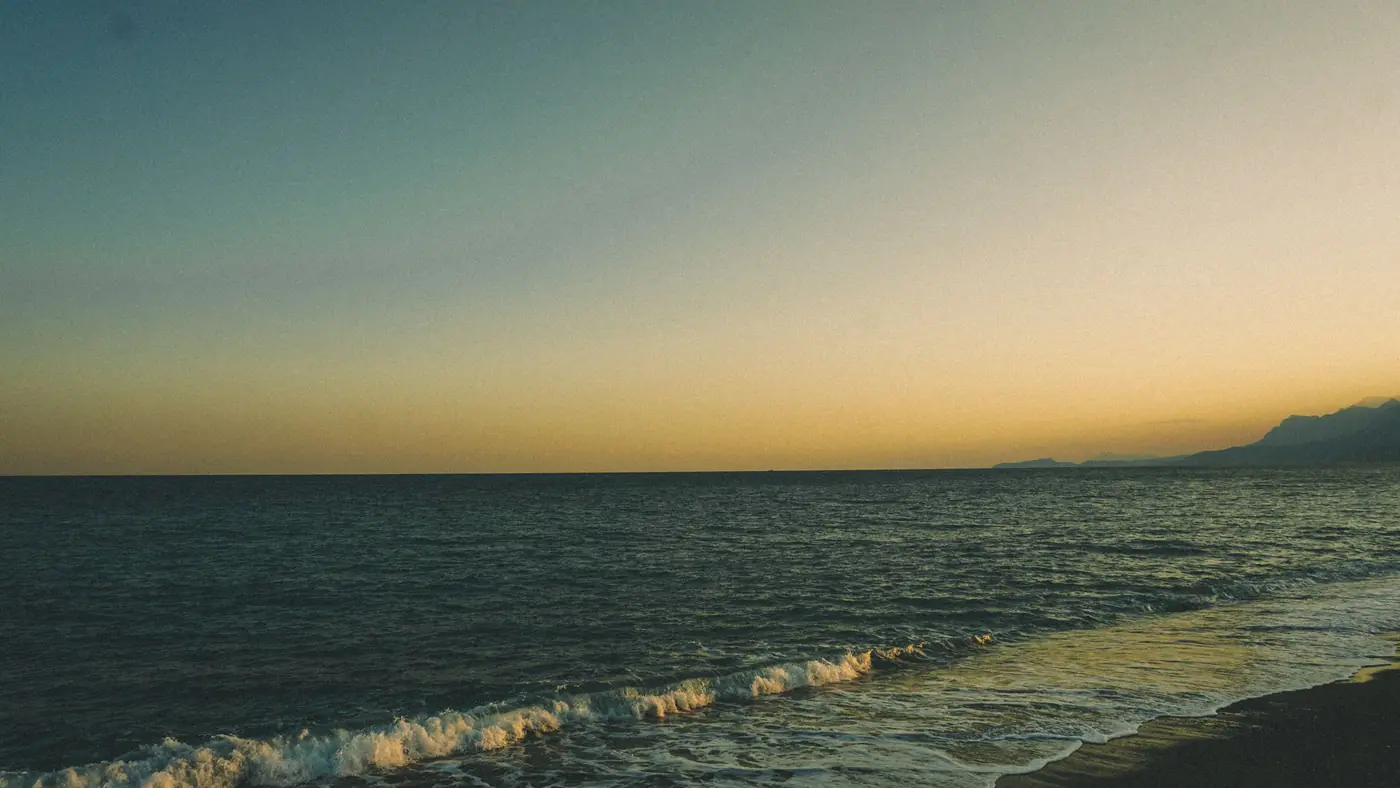 A tranquil view of the Antalya coast at sunset with gentle waves on the shore.