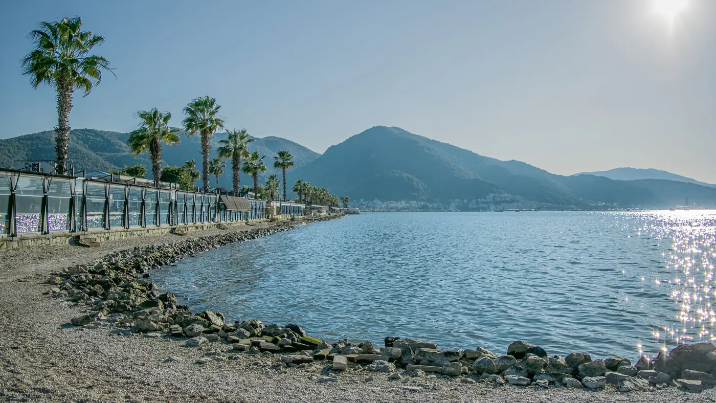 Sunny beach with palm trees and mountains in Fethiye, Türkiye.