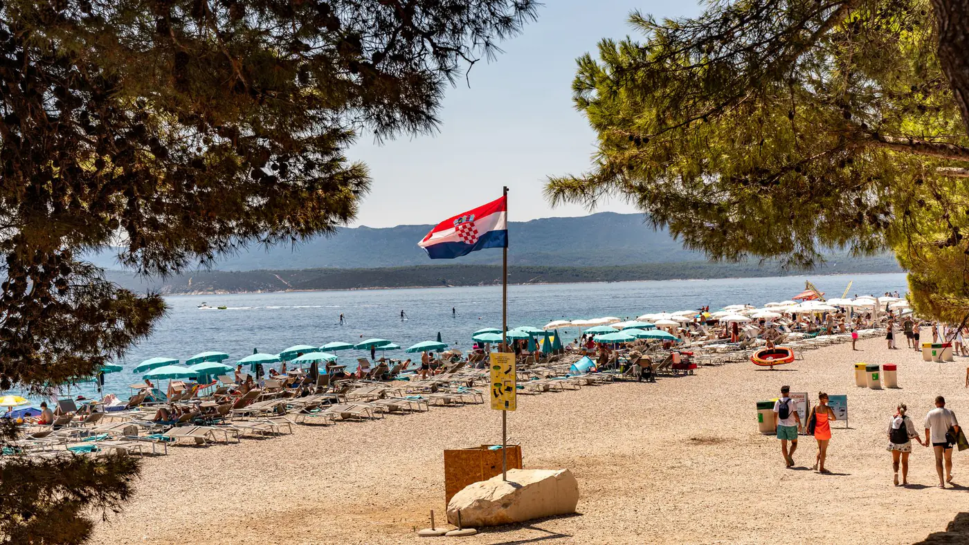 A vibrant summer scene at Zlatni Rat beach with clear blue water and beachgoers enjoying the sun.