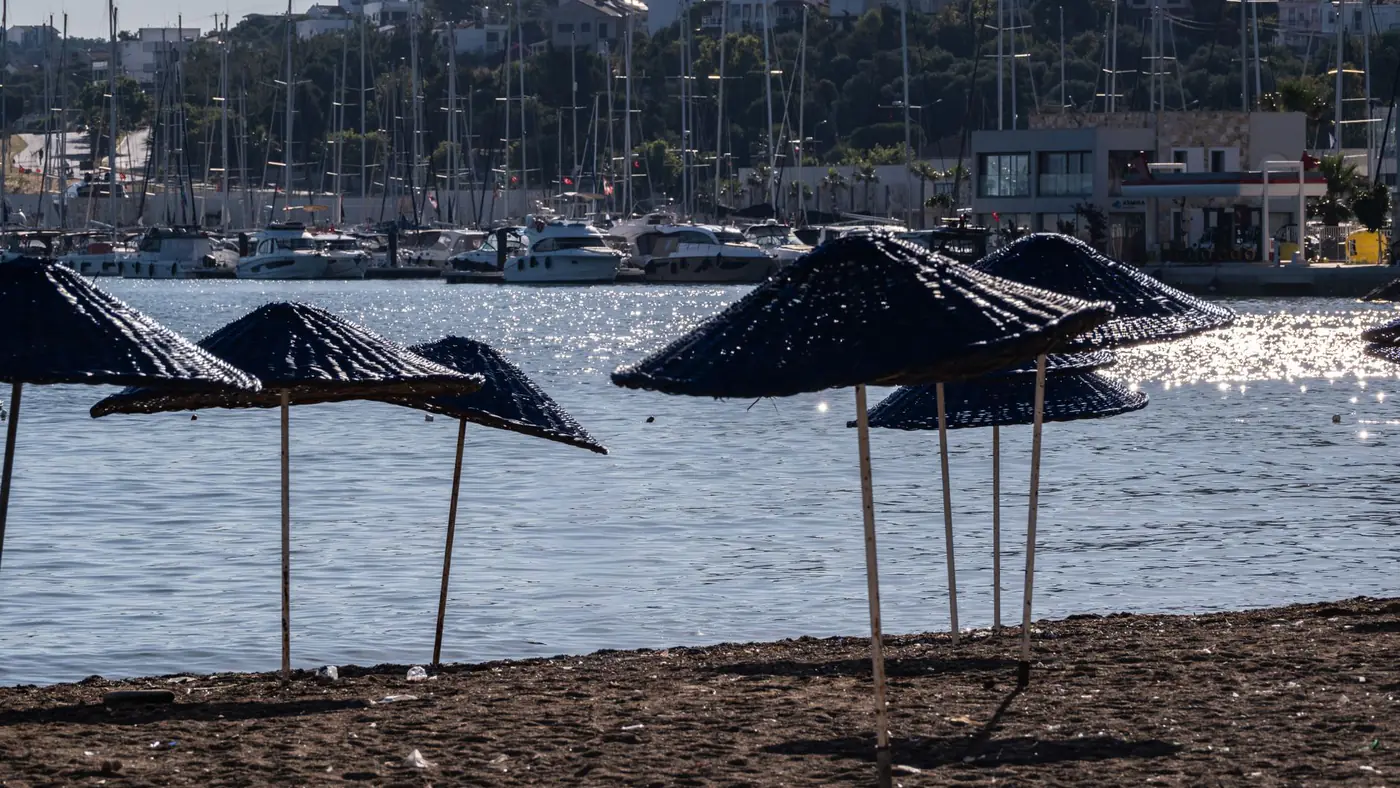 Tranquil beachfront scene with umbrellas and marina view in Foça, İzmir, Türkiye.