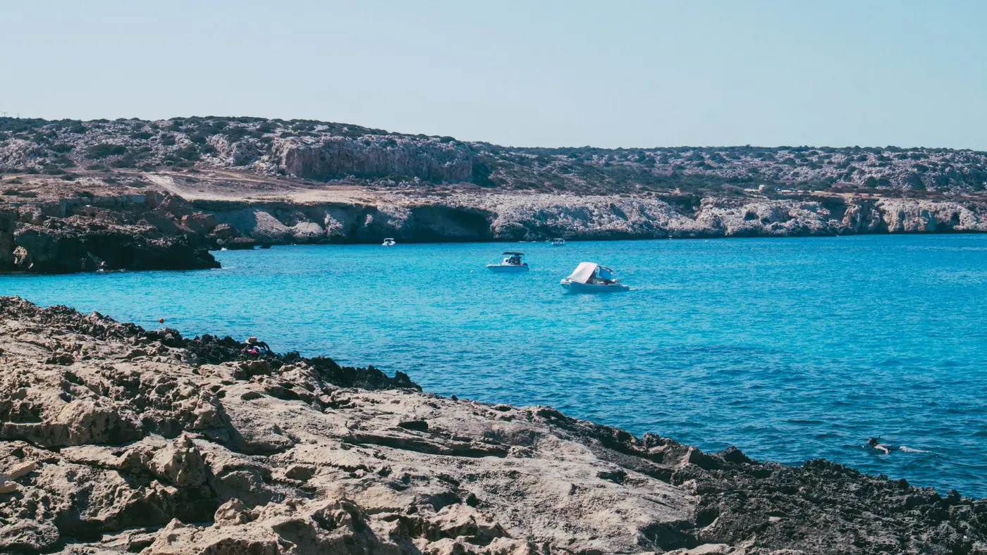 Picturesque view of a rocky coastline with boats on a serene blue sea.
