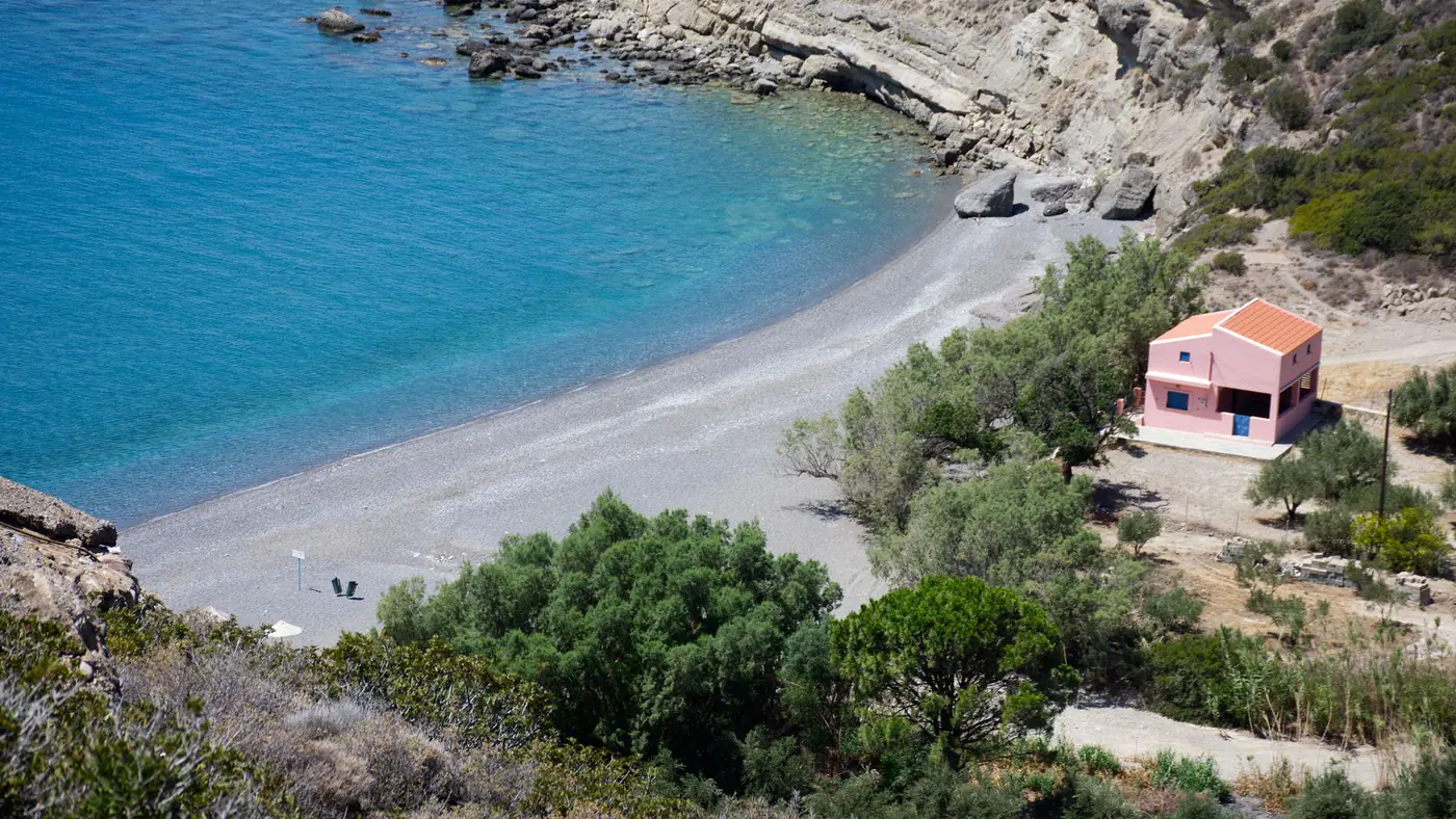 Aerial view of a serene beach with turquoise waters and a quaint pink house by the shore.