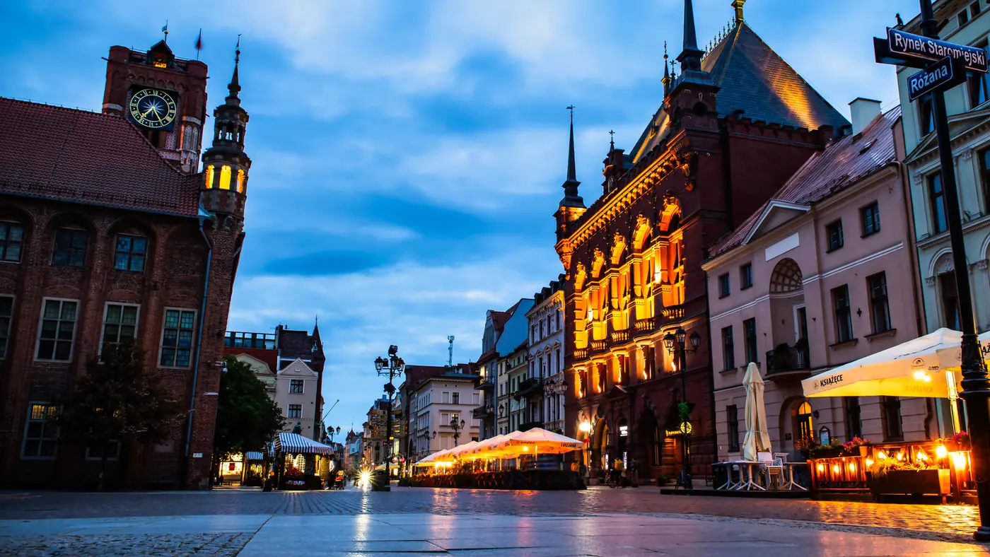 Vibrant twilight view of a historic town square with illuminated buildings and cobblestone streets.