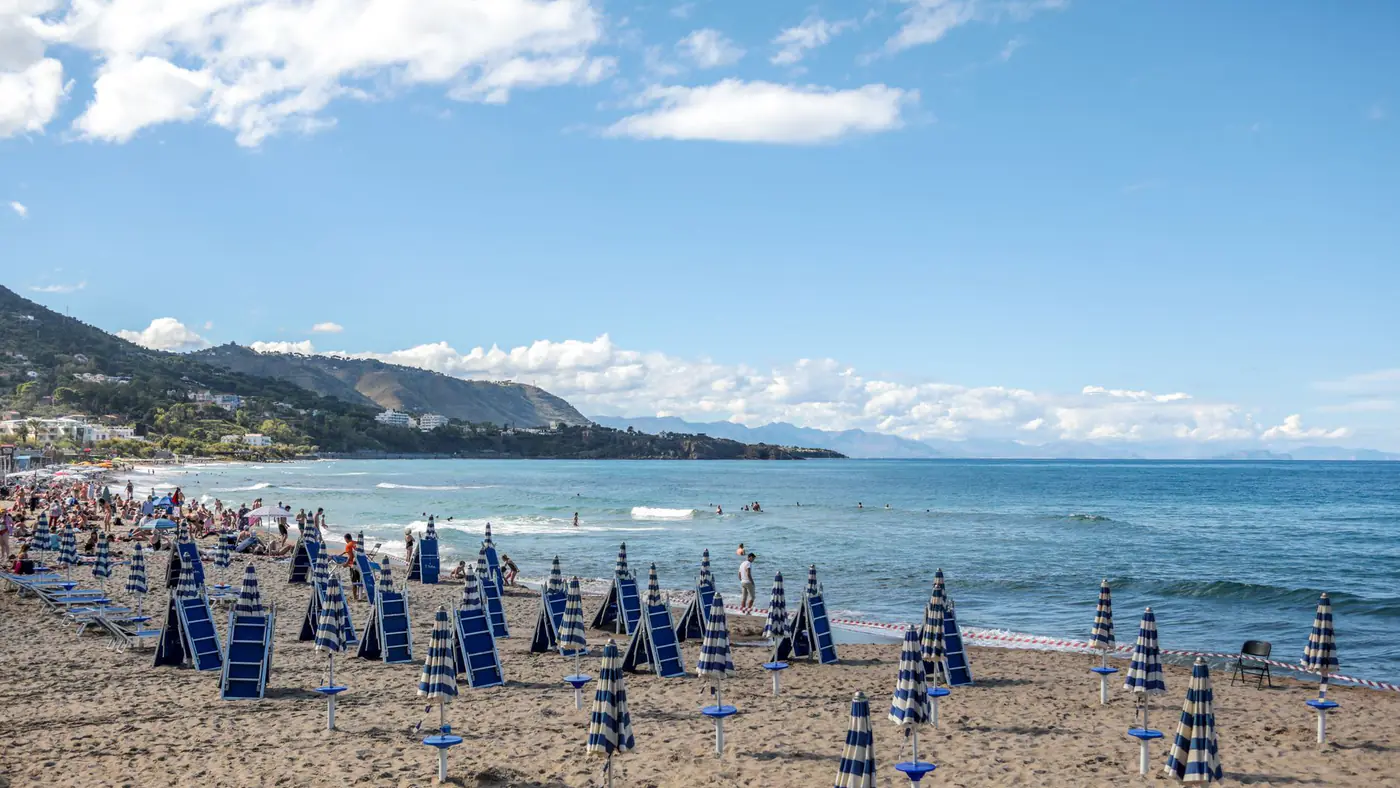 A scenic beach in Sicily, Italy, with rows of umbrellas and people enjoying the sun and sea.